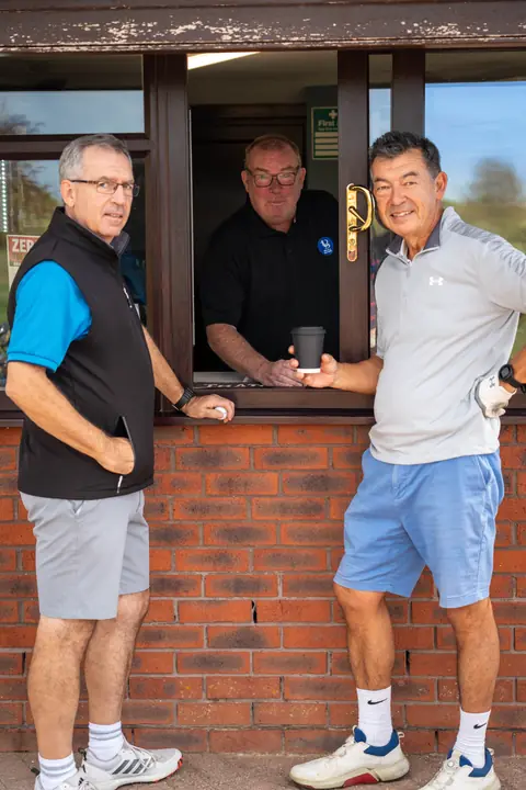 Members chatting at the clubhouse hatch with a coffee