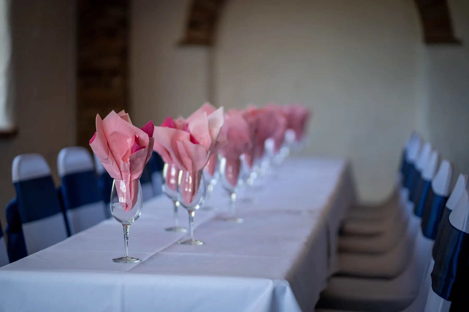 Pink napkins in wine glasses along a long table