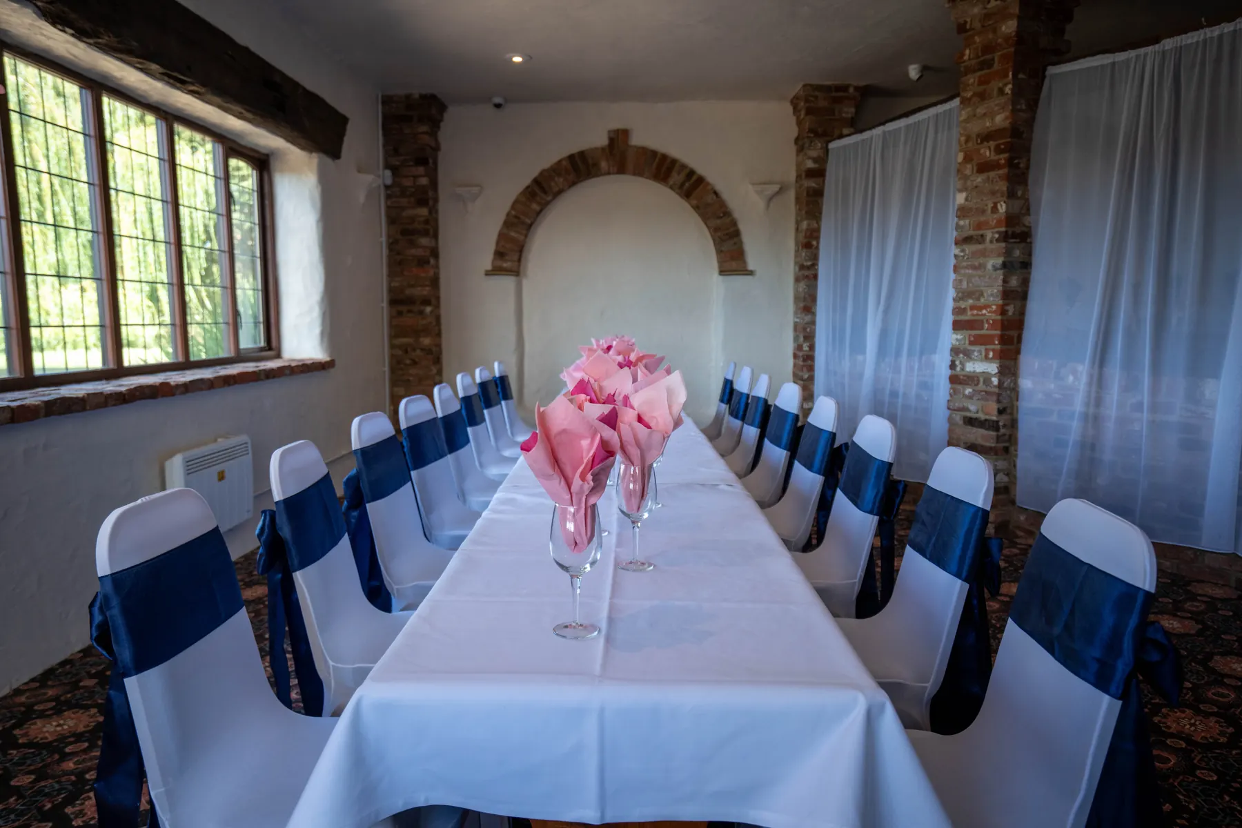 A long table with pink napkins beneath leaded windows