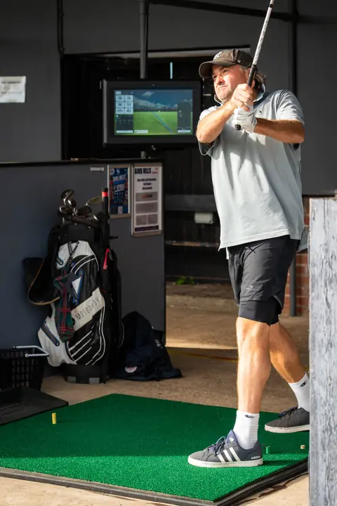 A golfer mid-swing in a TrackMan bay on the floodlit range