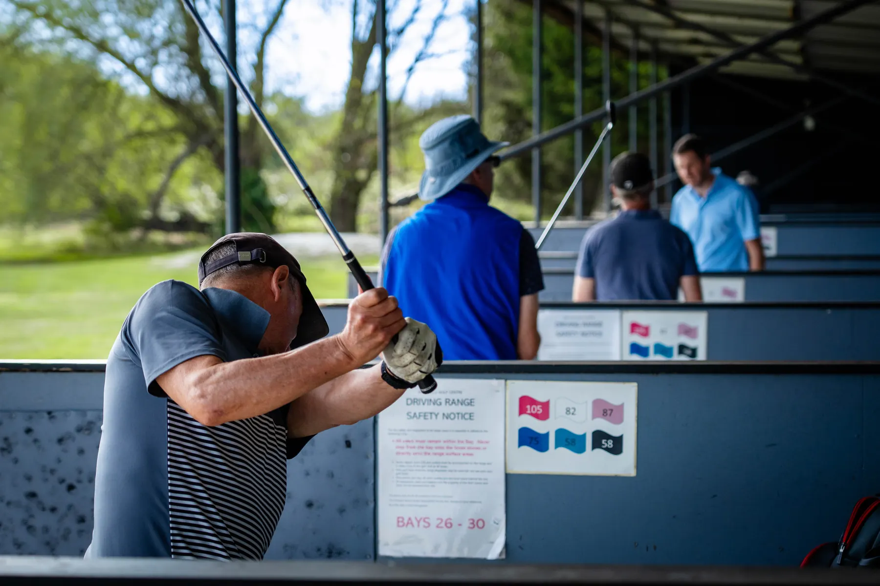 A golfer following through in a bay, other golfers practising behind