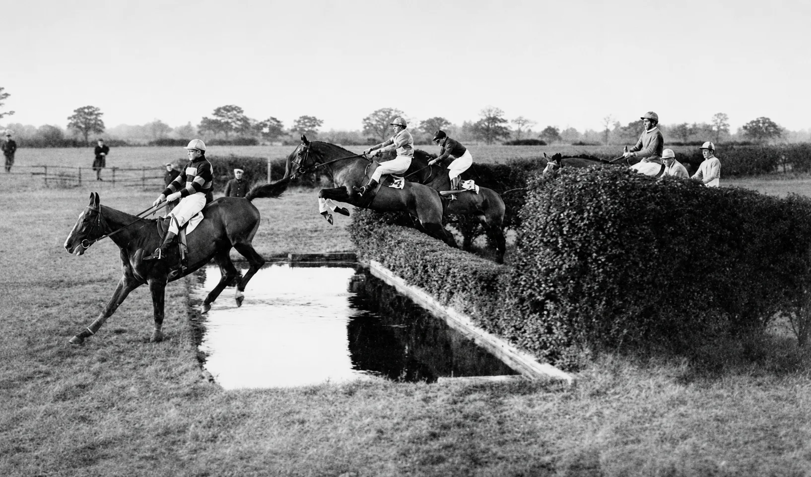 Riders taking the water jump at Hawthorn Hill, a field of steeplechasers over the hedge