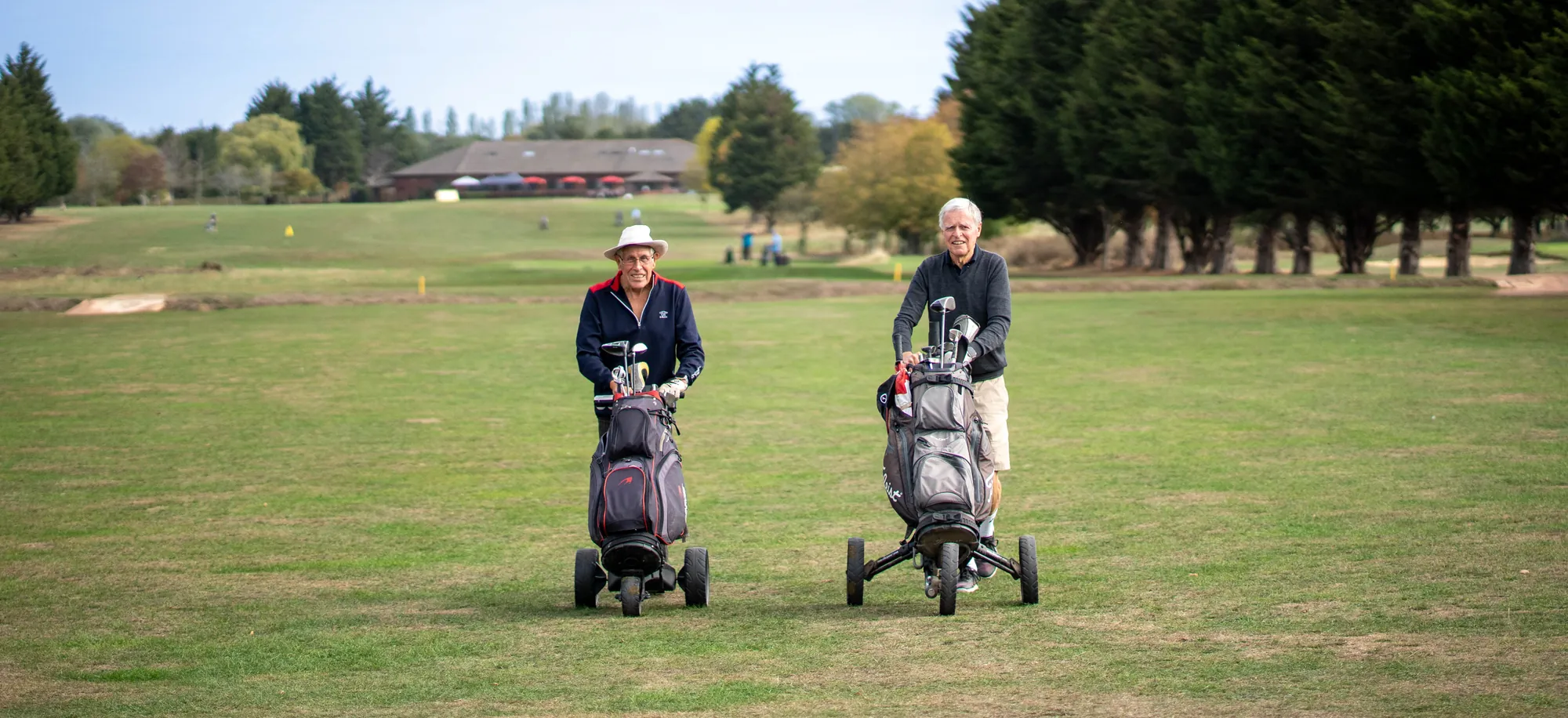 Two golfers walking down the fairway with their trolleys