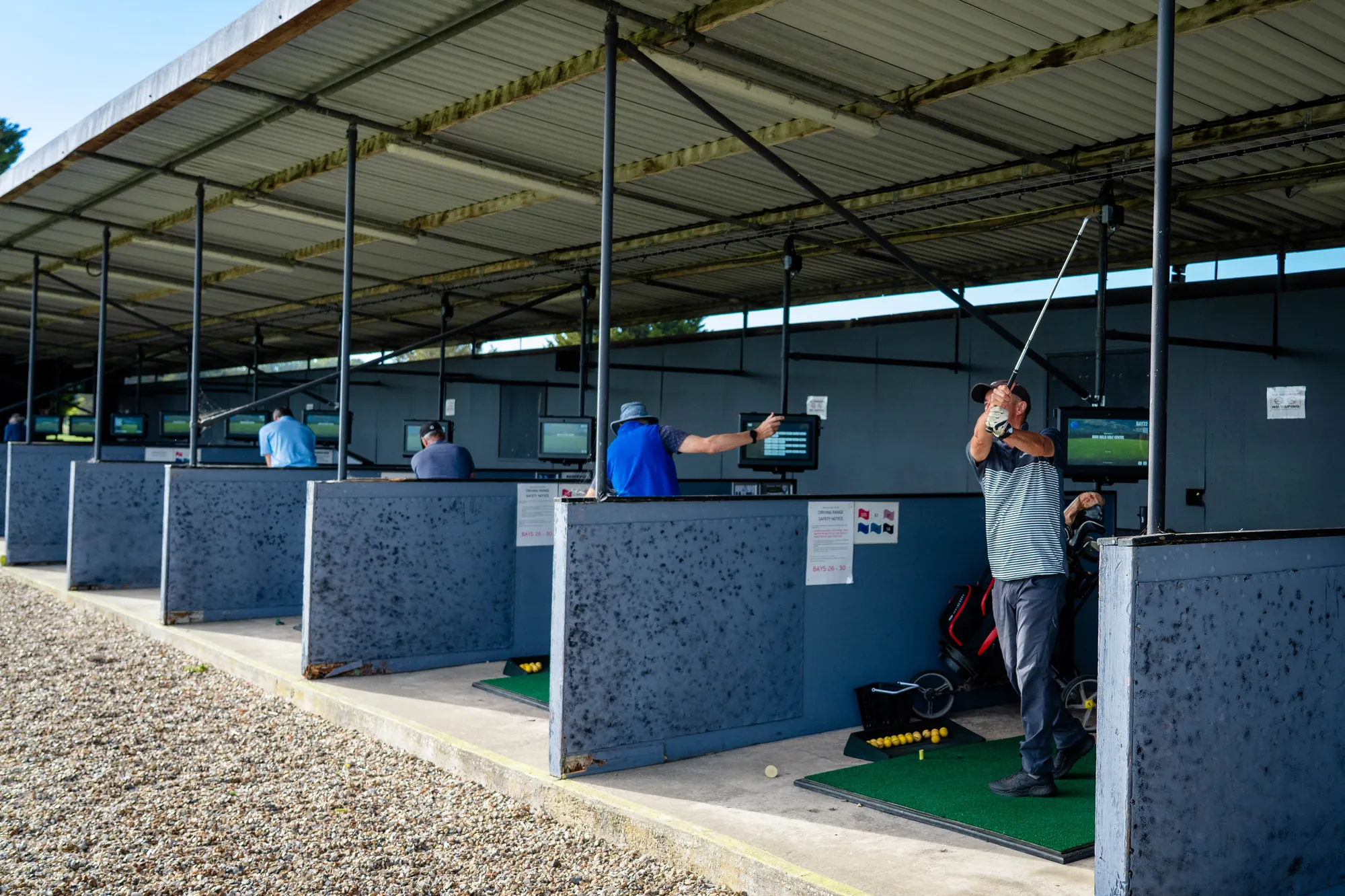 Golfers practising in the covered TrackMan bays at the driving range